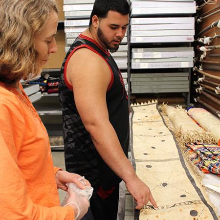 Fuavai examines a woven mat as his professor Holly Barker looks on