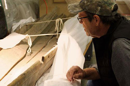 A man peers closely at the sides of the canoe