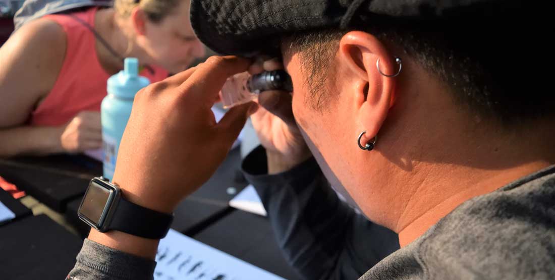 a dig participant looks at a microfossil through a magnifier