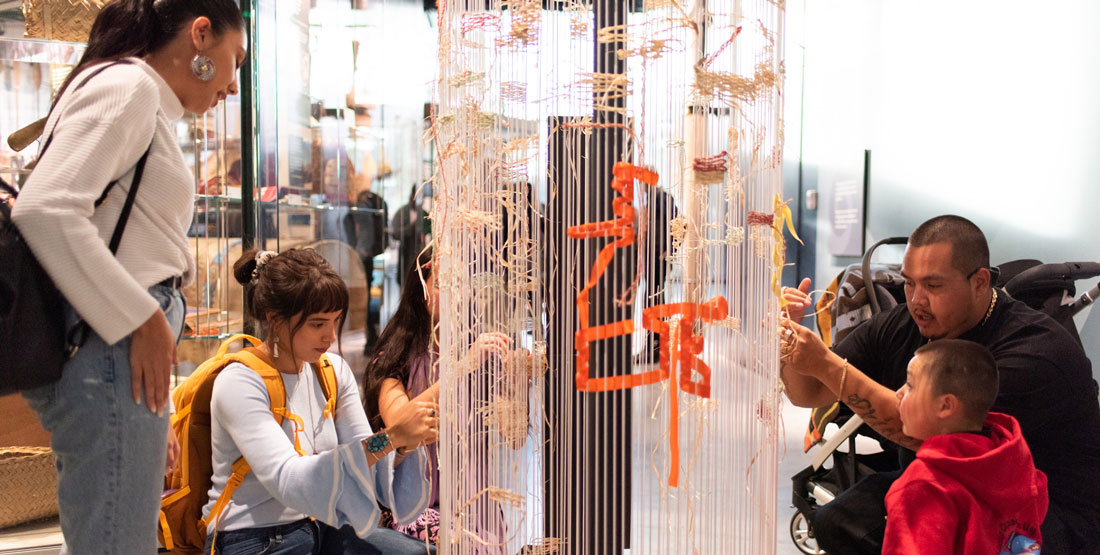 people weave ribbon and yarn on a community interactive exhibit