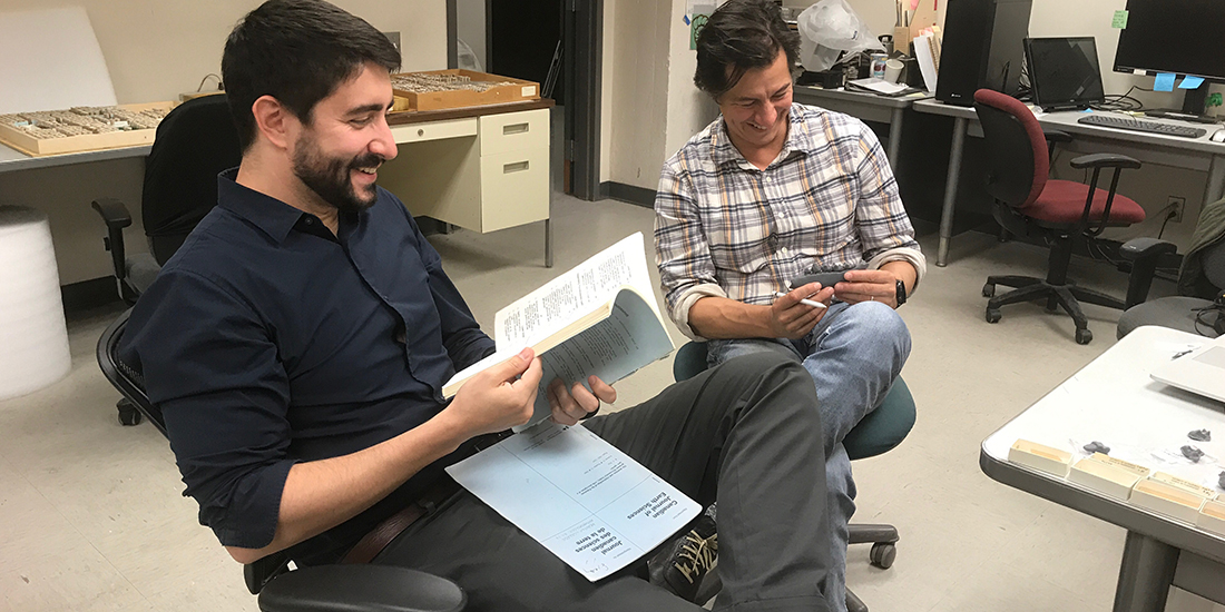 Two men sit in a lab looking at fossils