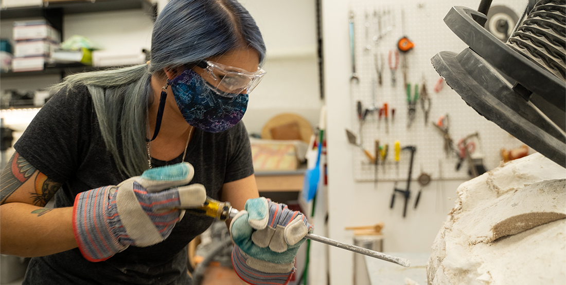 A woman uses a large screwdriver to pry open a plaster-covered fossil jacket