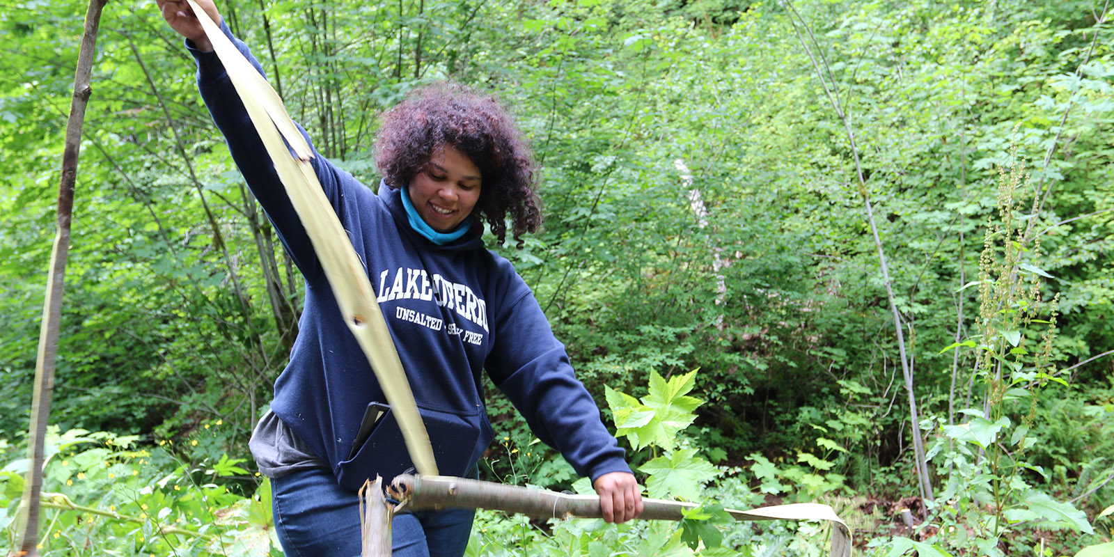 A woman strips bark from a branch