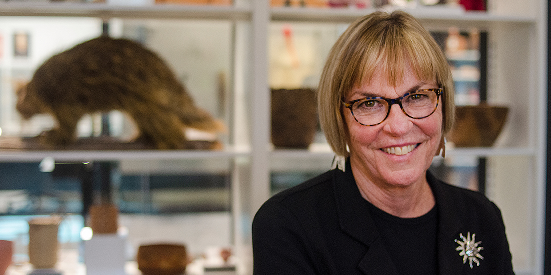 A woman smiles at the camera with collections on shelves behind her