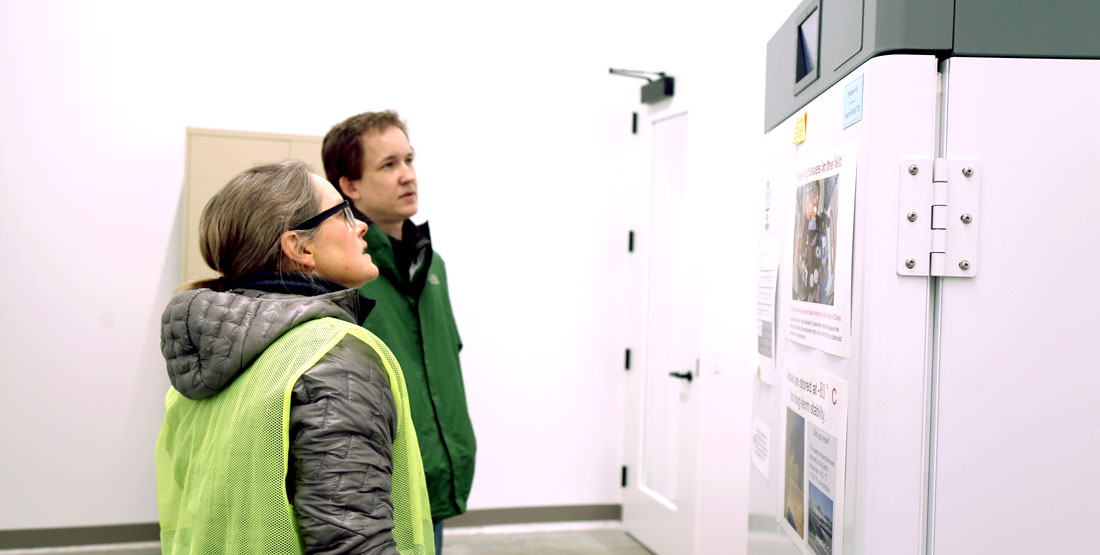 a woman and a man stand looking up at a freezer's digital screen