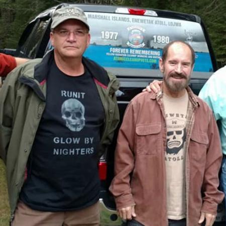 two men stand next to each other in front of the bed of a pick up truck