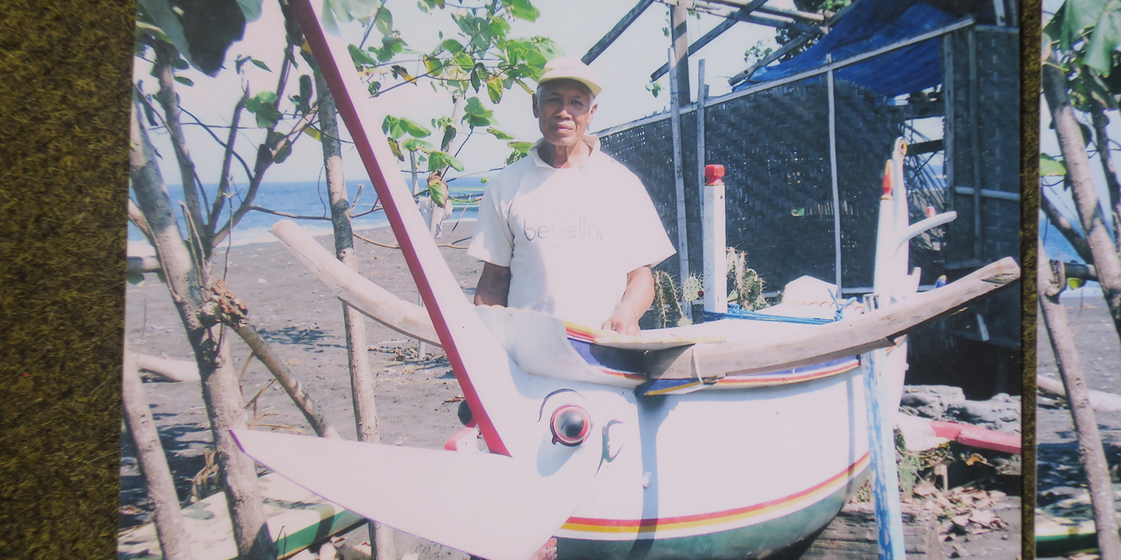 A man in a hat stands in front of a boat decorated with an eyeball and earings 