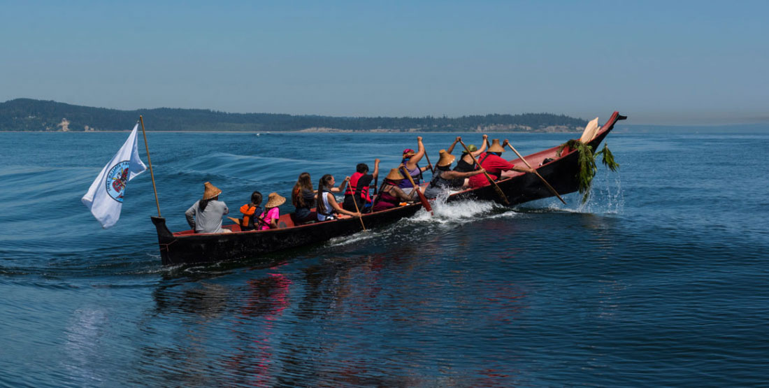 people paddle a canoe over a large wave during a canoe journey