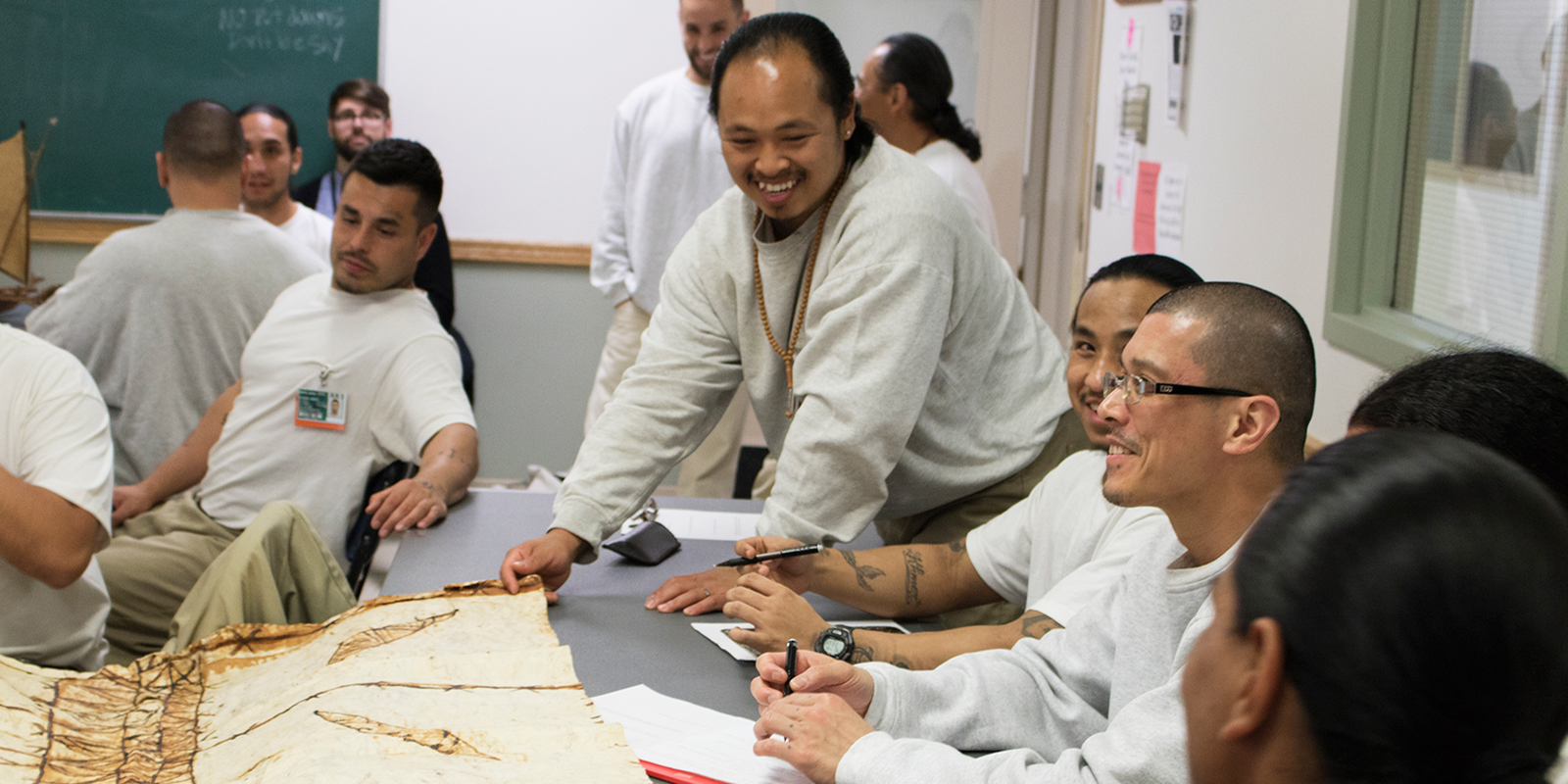 a group of men examine a tapa cloth