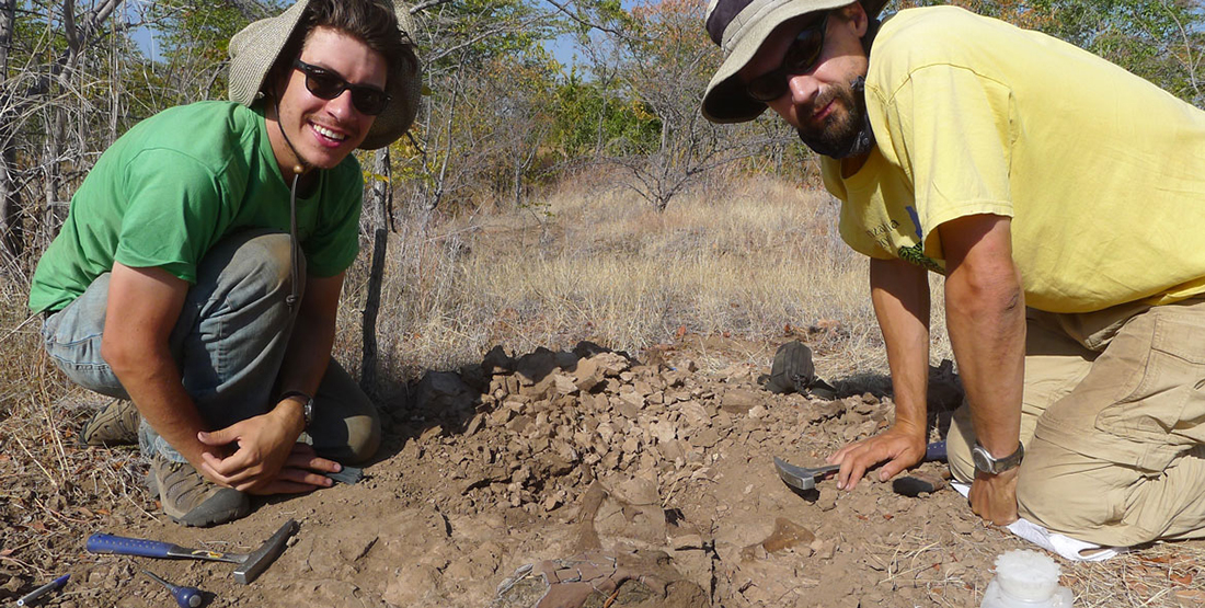 two men kneel next to fossil in the ground