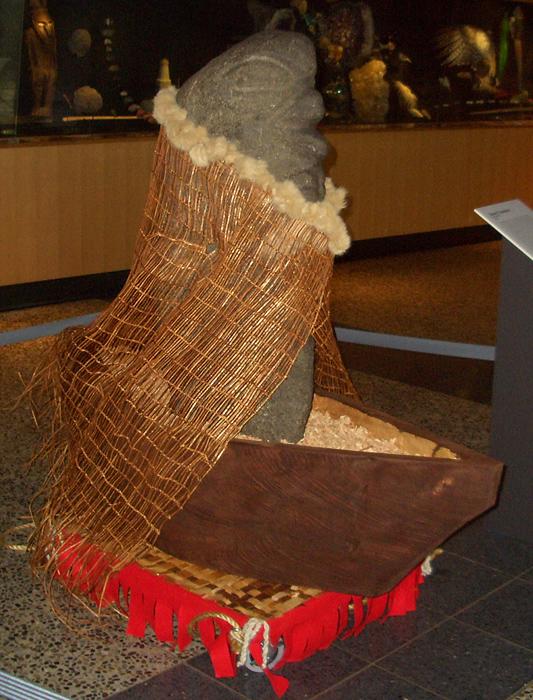 A stone statue with a woven robe sits in a boat inside of a room