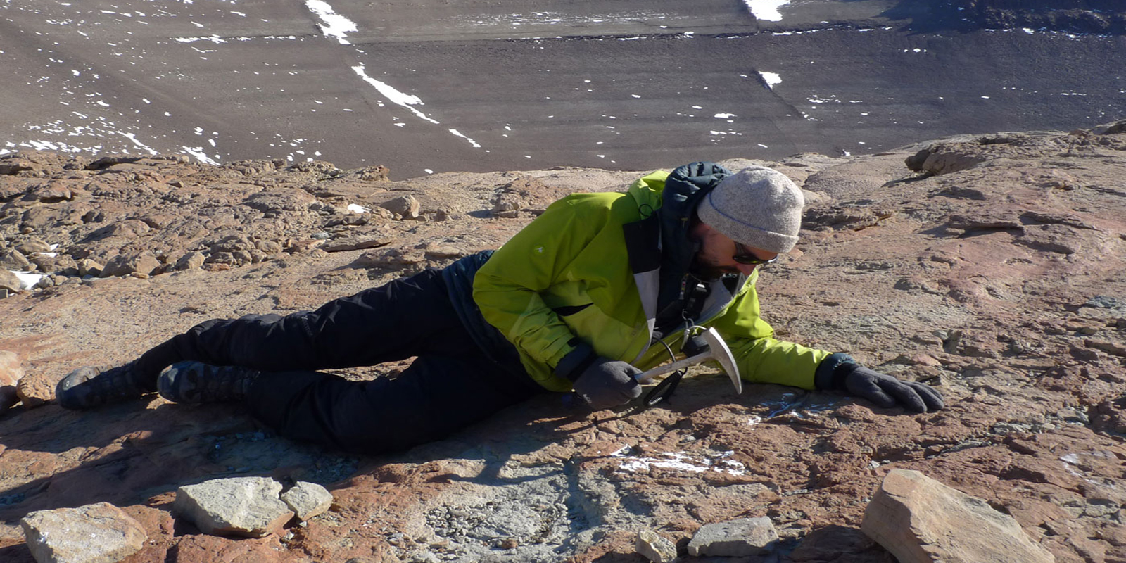 a man lays on the rock while using a hammer to remove rock from the surface