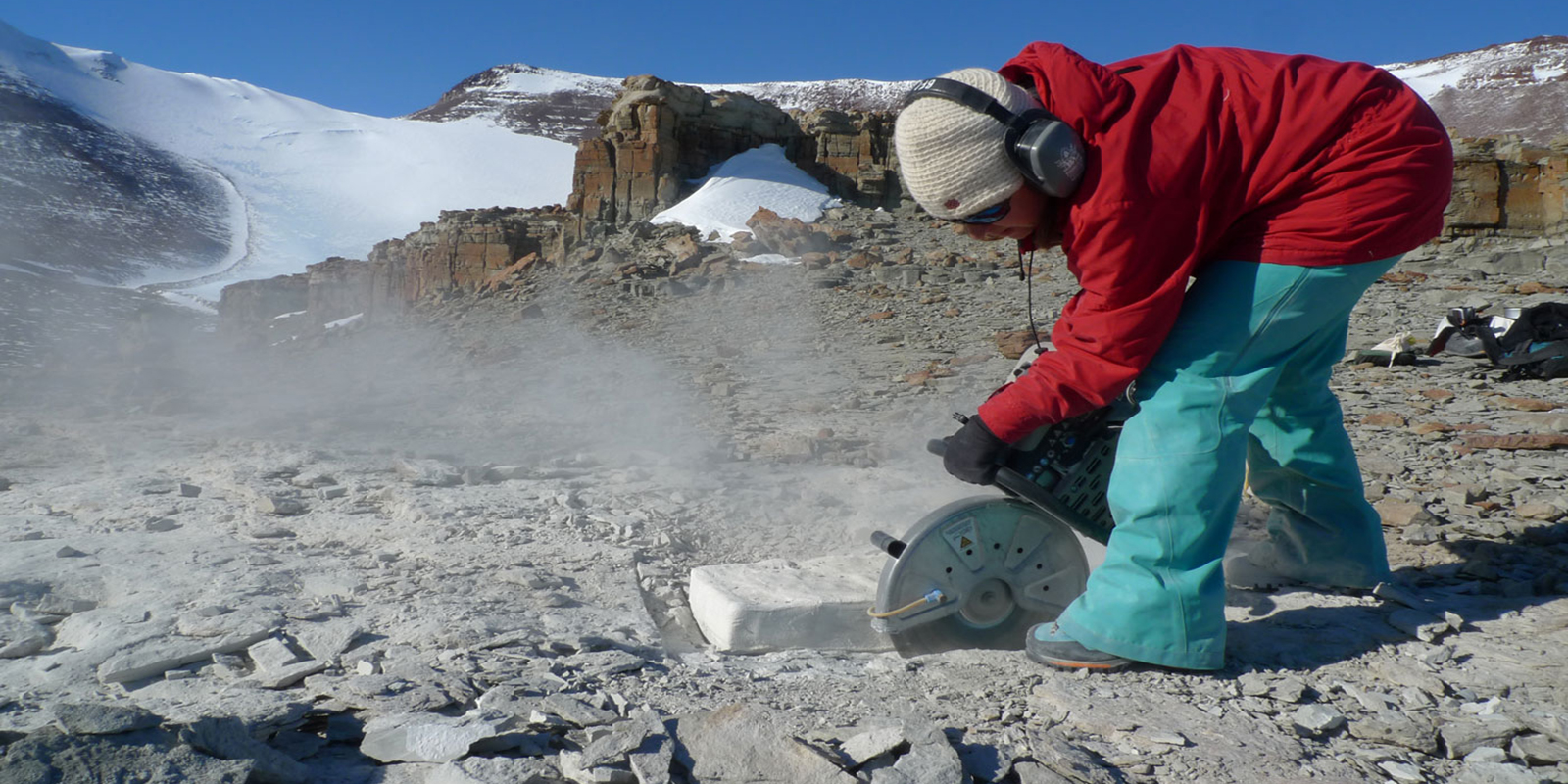 A young woman uses a rock saw to cut a pedestal around on fossil 